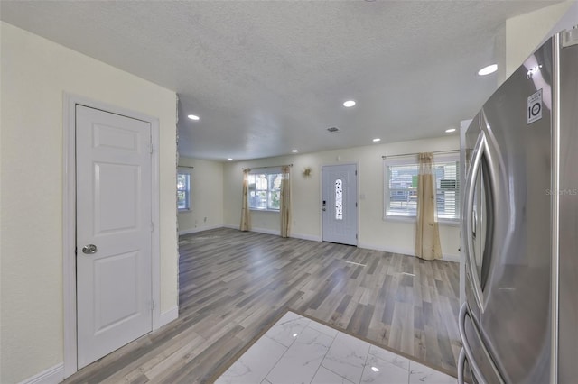 interior space featuring a textured ceiling, light wood finished floors, freestanding refrigerator, and baseboards