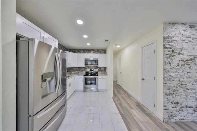 kitchen featuring visible vents, white cabinets, light stone counters, stainless steel appliances, and backsplash