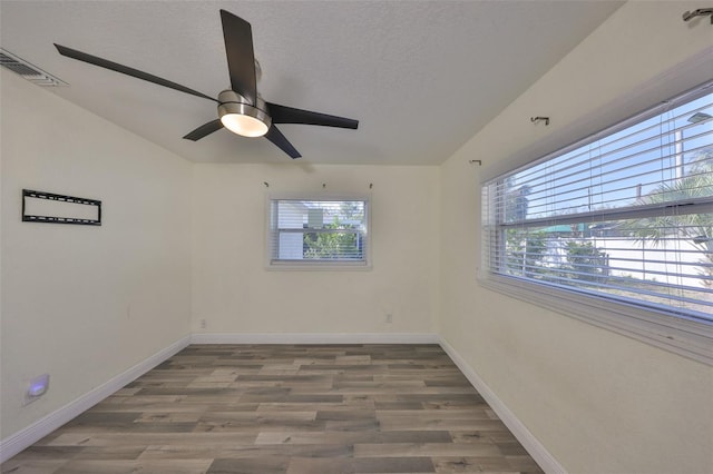 unfurnished room with plenty of natural light, baseboards, a textured ceiling, and wood finished floors