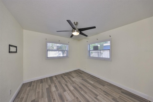 unfurnished room with a wealth of natural light, a textured ceiling, baseboards, and wood finished floors