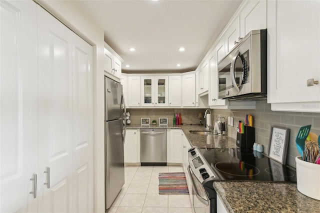 kitchen featuring tasteful backsplash, white cabinets, dark stone countertops, stainless steel appliances, and a sink