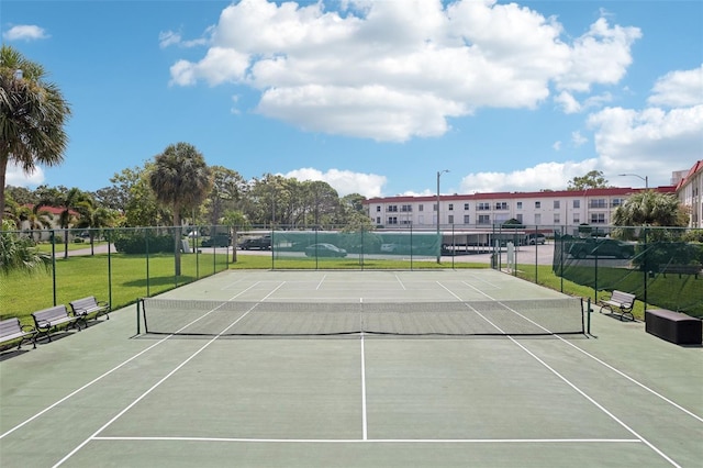 view of tennis court with a yard and fence