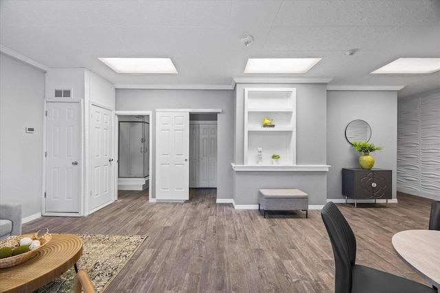 living area featuring built in shelves, visible vents, baseboards, and wood finished floors