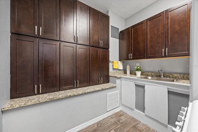 kitchen with wood tiled floor, visible vents, a sink, and dark brown cabinetry