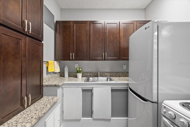 kitchen featuring light stone countertops, white appliances, dark brown cabinets, and a sink