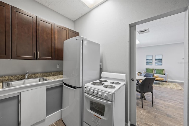 kitchen with dark brown cabinetry, white appliances, visible vents, light wood-style floors, and a sink