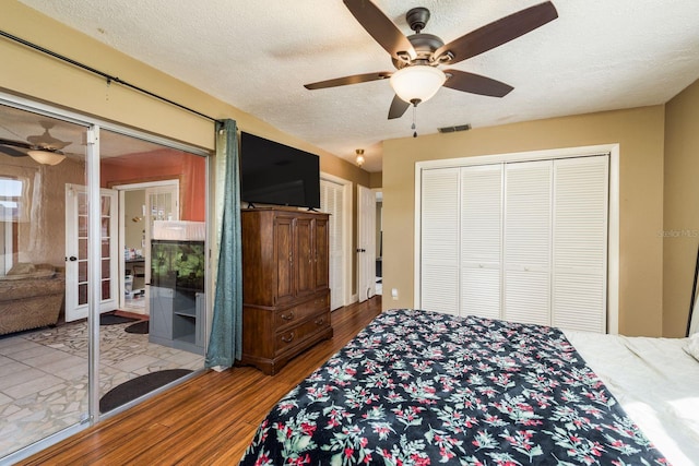 bedroom with a textured ceiling, ceiling fan, wood finished floors, visible vents, and french doors