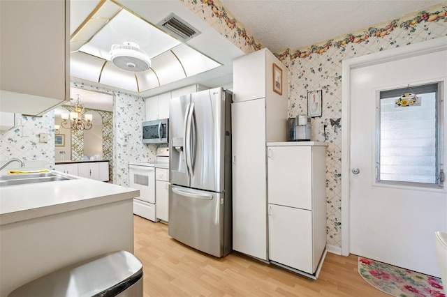 kitchen featuring stainless steel appliances, a sink, visible vents, light wood-style floors, and wallpapered walls