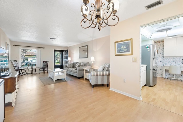 living room featuring light wood finished floors, visible vents, a textured ceiling, a chandelier, and baseboards