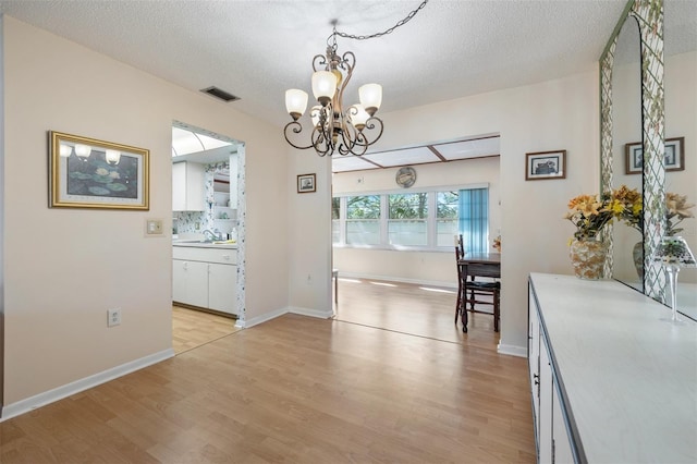 unfurnished dining area with light wood-type flooring, a sink, visible vents, and an inviting chandelier