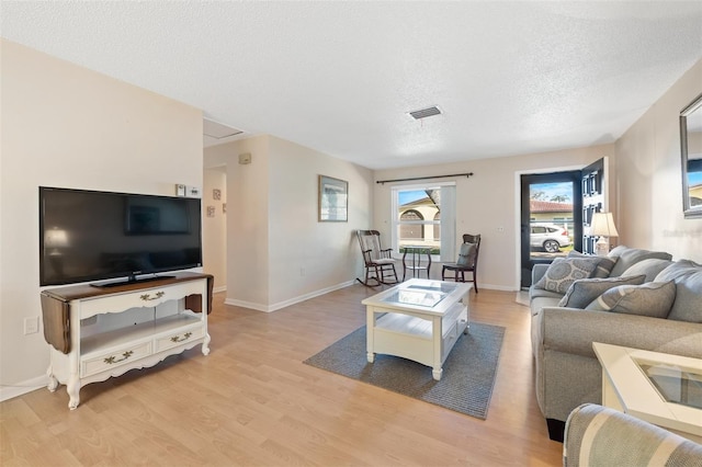 living area with light wood finished floors, baseboards, visible vents, and a textured ceiling