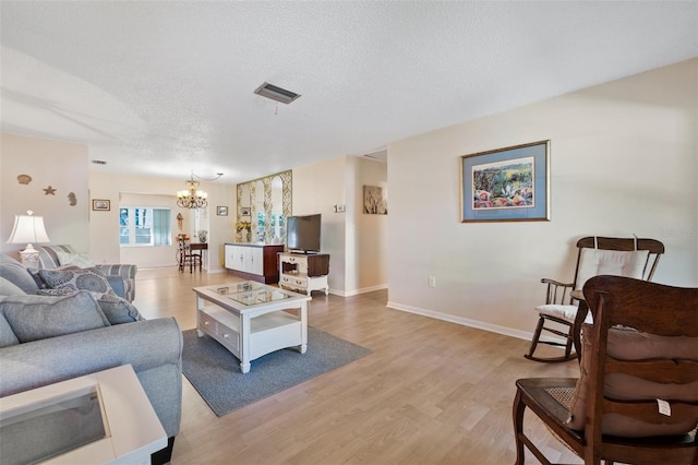 living room featuring a textured ceiling, light wood-style flooring, a notable chandelier, visible vents, and baseboards