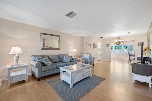 living room featuring a textured ceiling, light wood-style floors, visible vents, and an inviting chandelier