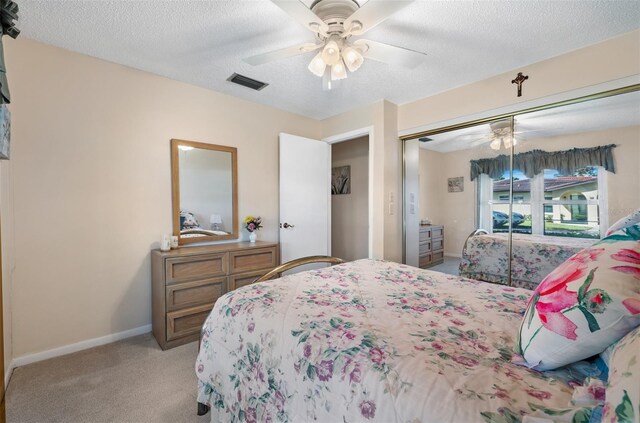 bedroom featuring a textured ceiling, light carpet, visible vents, baseboards, and a closet