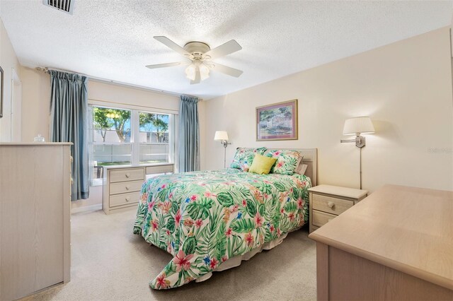 bedroom featuring light carpet, a textured ceiling, visible vents, and a ceiling fan