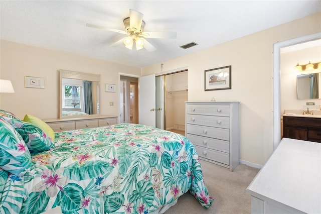 bedroom with a closet, visible vents, light carpet, a sink, and ensuite bath