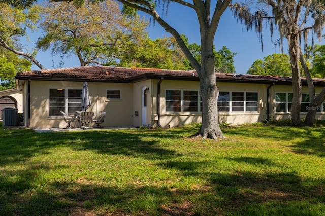 rear view of property featuring a yard, central AC unit, and stucco siding