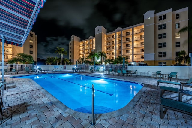 pool at twilight featuring a patio area, a community pool, and fence