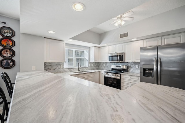 kitchen with light stone counters, stainless steel appliances, a sink, visible vents, and decorative backsplash