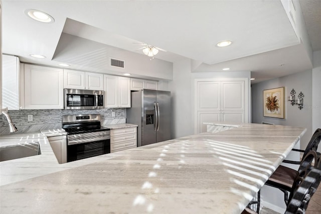 kitchen with light stone countertops, a sink, visible vents, appliances with stainless steel finishes, and decorative backsplash