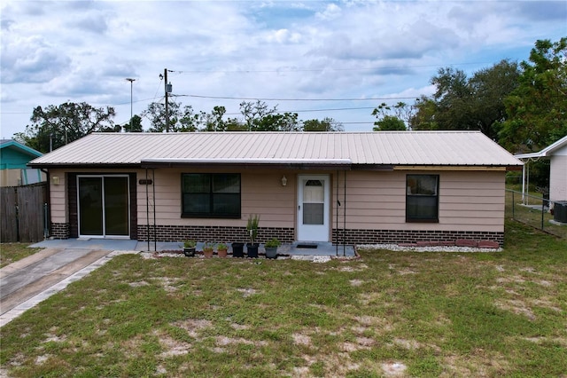 ranch-style house with metal roof, central air condition unit, brick siding, fence, and a front lawn