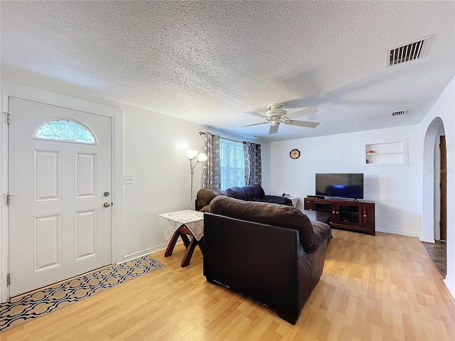 living area with arched walkways, ceiling fan, light wood-type flooring, and visible vents