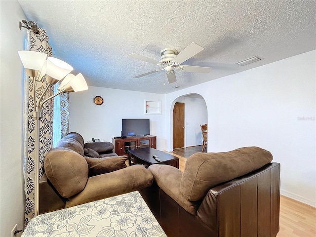 living room featuring a ceiling fan, arched walkways, light wood-type flooring, and a textured ceiling