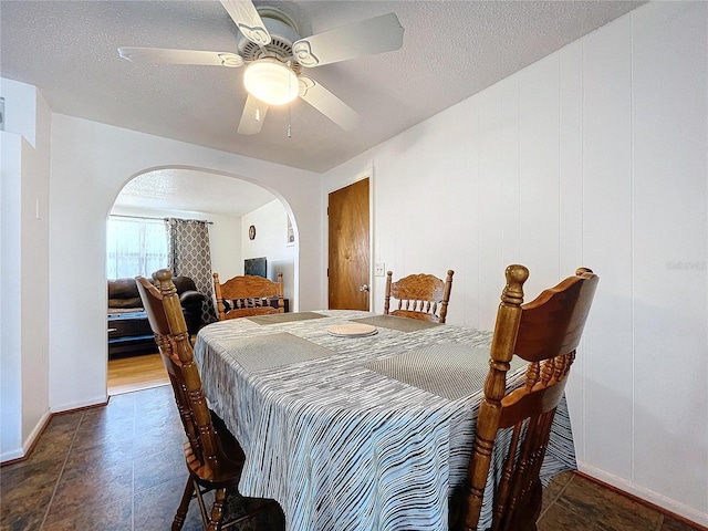 dining space with a ceiling fan, arched walkways, and a textured ceiling