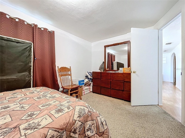 bedroom featuring arched walkways, a textured ceiling, carpet flooring, and visible vents