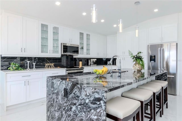 kitchen with a breakfast bar area, stainless steel appliances, white cabinets, marble finish floor, and tasteful backsplash