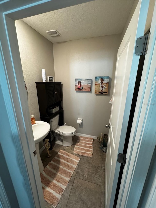 half bath featuring visible vents, toilet, a textured ceiling, baseboards, and tile patterned floors