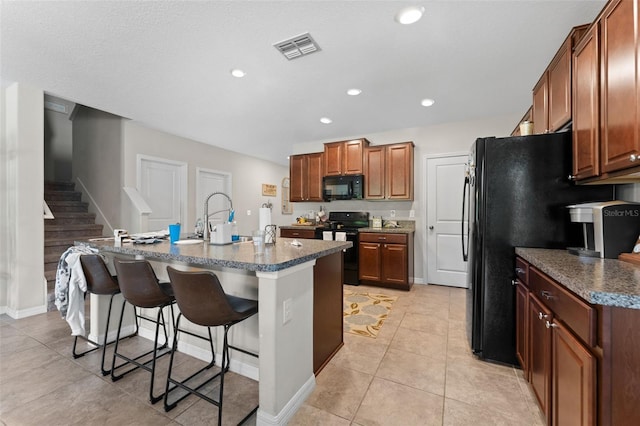 kitchen with a kitchen breakfast bar, a sink, visible vents, an island with sink, and black appliances