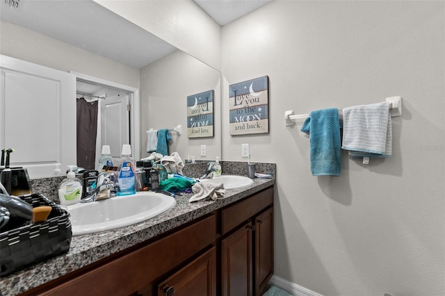 bathroom featuring double vanity, baseboards, and a sink