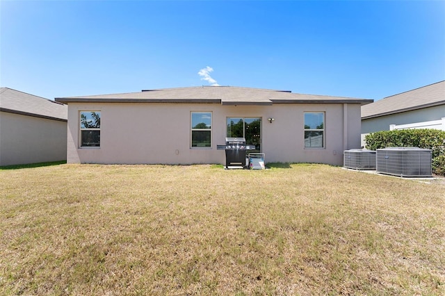 rear view of house with a lawn, central air condition unit, and stucco siding