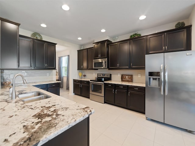 kitchen featuring decorative backsplash, light stone counters, stainless steel appliances, and a sink