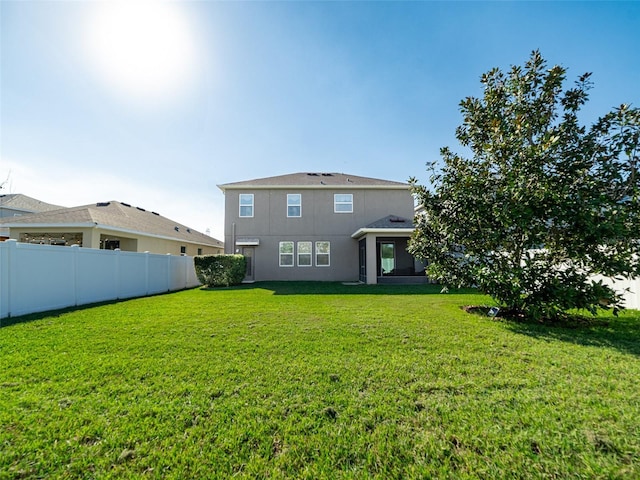 rear view of house featuring a lawn, fence, and stucco siding