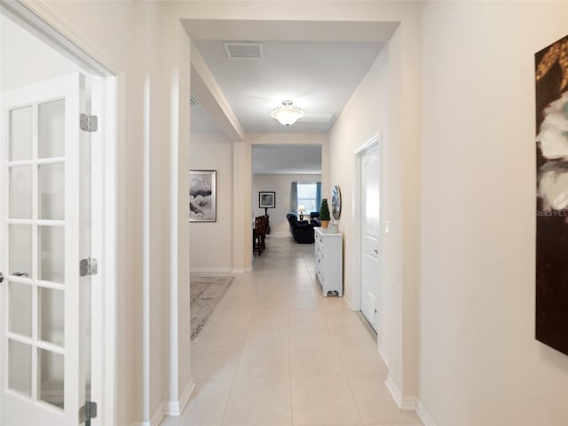 hall featuring light tile patterned floors, baseboards, and visible vents