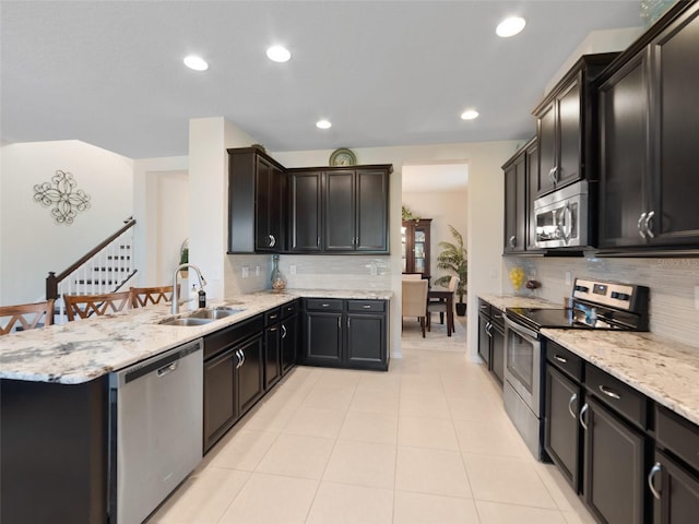 kitchen with appliances with stainless steel finishes, a sink, a peninsula, and light stone countertops