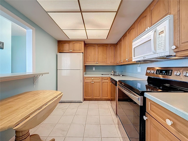 kitchen featuring brown cabinets, a sink, appliances with stainless steel finishes, light countertops, and light tile patterned floors