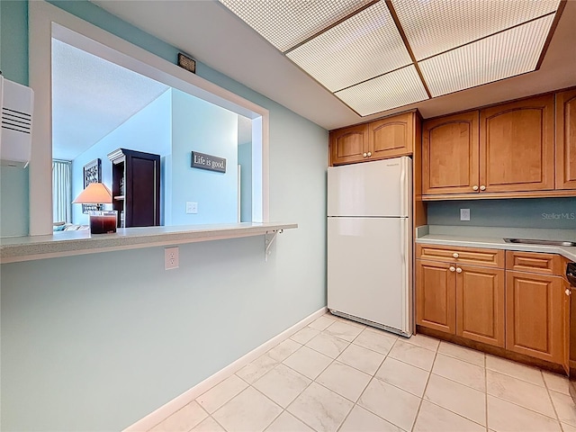 kitchen featuring light tile patterned floors, baseboards, freestanding refrigerator, light countertops, and brown cabinets