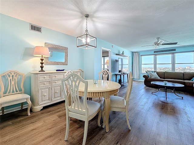 dining room featuring visible vents, ceiling fan with notable chandelier, a textured ceiling, and hardwood / wood-style flooring