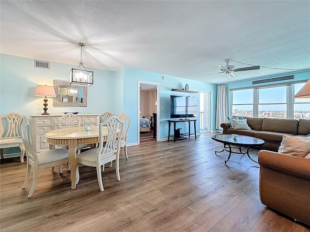 dining space with visible vents, ceiling fan with notable chandelier, a textured ceiling, hardwood / wood-style floors, and baseboards