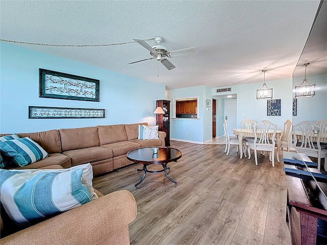 living room featuring visible vents, a ceiling fan, a textured ceiling, light wood-style floors, and baseboards