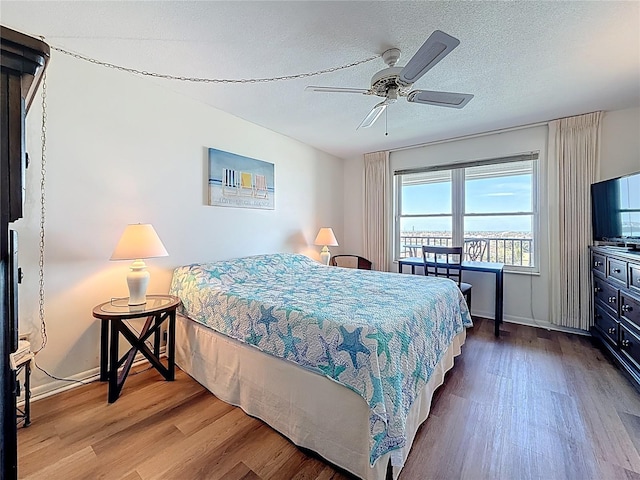 bedroom with ceiling fan, wood finished floors, baseboards, and a textured ceiling