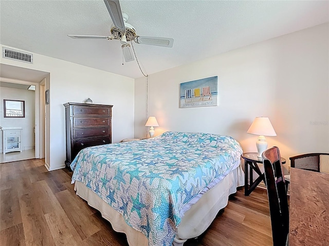 bedroom featuring visible vents, a textured ceiling, ceiling fan, and wood finished floors