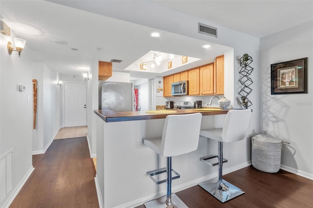 kitchen featuring dark wood-style floors, stainless steel appliances, a kitchen bar, visible vents, and baseboards