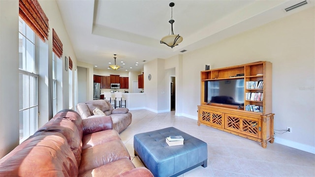 living room featuring a tray ceiling, visible vents, baseboards, and light tile patterned flooring