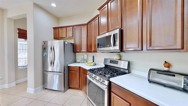 kitchen featuring light countertops, appliances with stainless steel finishes, brown cabinetry, and light tile patterned flooring