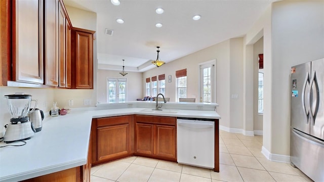 kitchen featuring visible vents, freestanding refrigerator, white dishwasher, a sink, and a peninsula