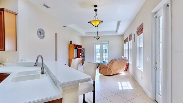 kitchen featuring light tile patterned floors, visible vents, a raised ceiling, light countertops, and a sink